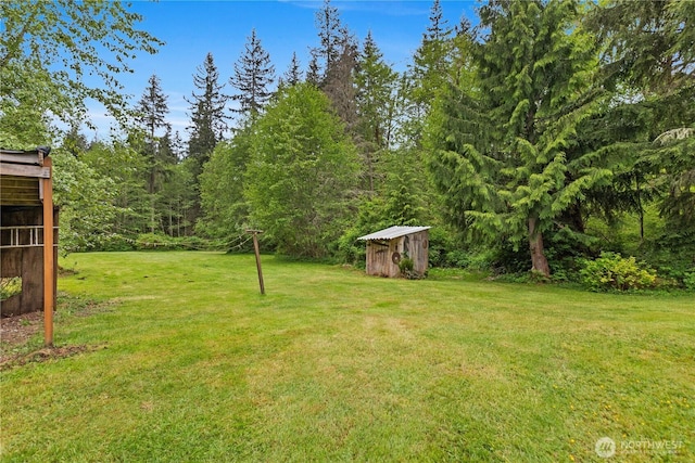 view of green lawn featuring a shed, an outdoor structure, and a forest view