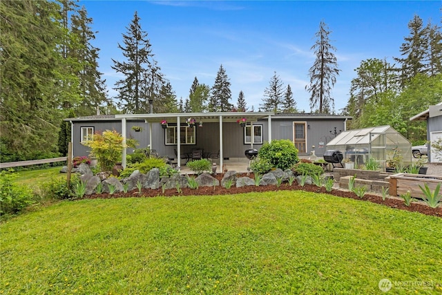 rear view of property featuring a greenhouse, a lawn, an outdoor structure, and a patio