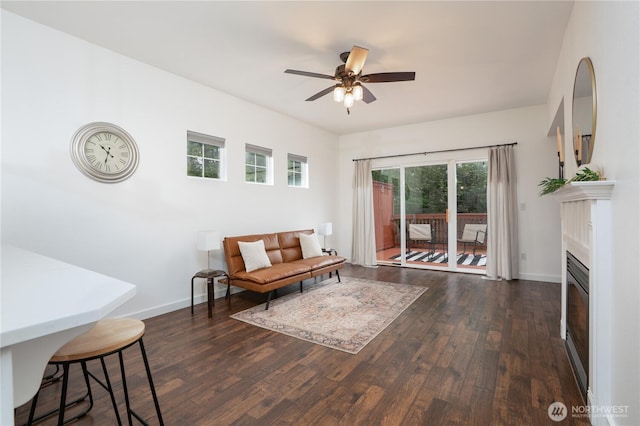 living area featuring baseboards, a ceiling fan, dark wood finished floors, and a glass covered fireplace