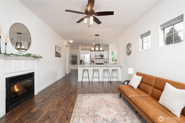 living area featuring dark wood-type flooring, baseboards, ceiling fan, and a glass covered fireplace