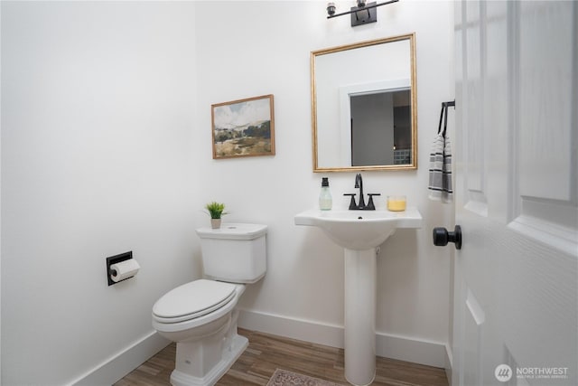 half bathroom featuring toilet, baseboards, a sink, and wood finished floors