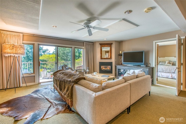 carpeted living room featuring a glass covered fireplace and ceiling fan