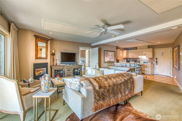 living room featuring light tile patterned flooring, light carpet, a ceiling fan, baseboards, and a glass covered fireplace