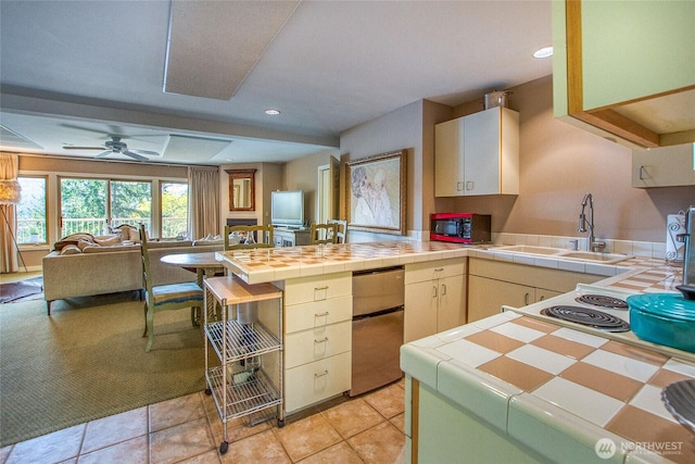 kitchen featuring refrigerator, a sink, a peninsula, open floor plan, and tile counters