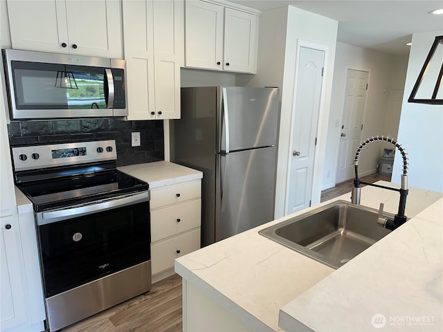 kitchen featuring a sink, light wood-type flooring, backsplash, white cabinets, and appliances with stainless steel finishes