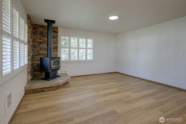 unfurnished living room with a wood stove, visible vents, wood finished floors, and baseboards
