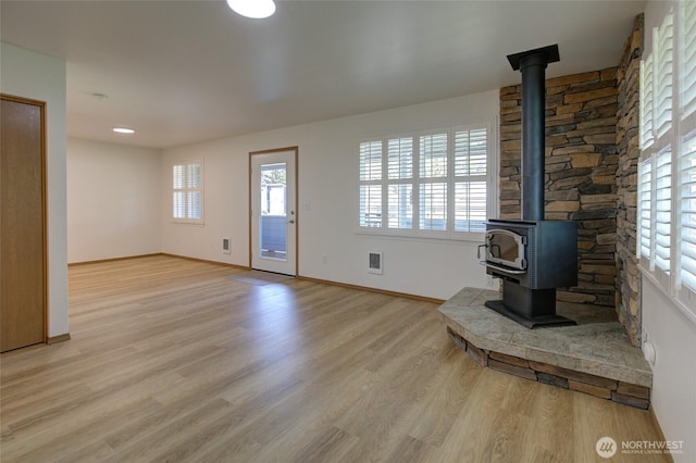 unfurnished living room with a wood stove, heating unit, baseboards, and light wood-type flooring