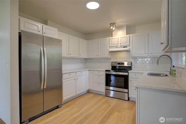 kitchen featuring under cabinet range hood, appliances with stainless steel finishes, backsplash, a sink, and light wood-type flooring
