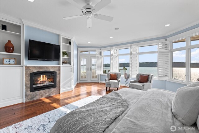 bedroom featuring wood finished floors, a tile fireplace, baseboards, french doors, and crown molding