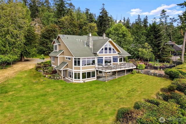back of house featuring a sunroom, a wooden deck, a lawn, and a chimney