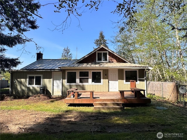 rear view of house with metal roof, a chimney, fence, and a deck