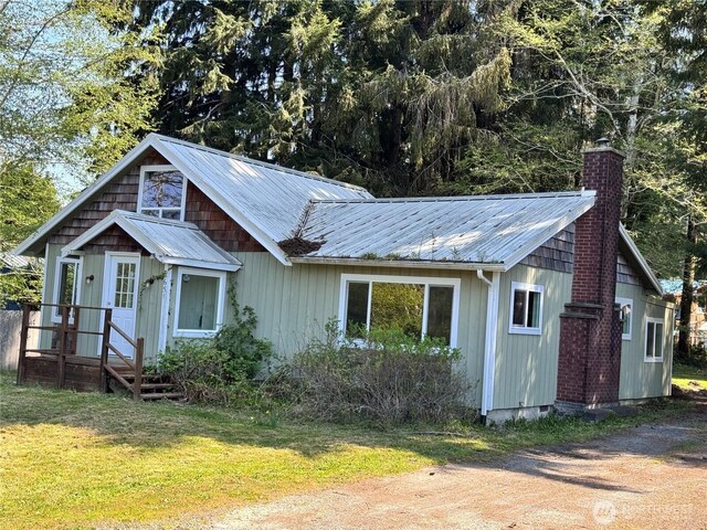 view of front of property featuring a front lawn, a chimney, and metal roof