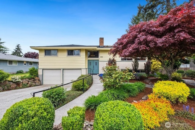 bi-level home with an attached garage, driveway, and a chimney