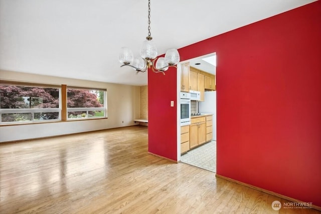 interior space featuring hanging light fixtures, an inviting chandelier, white appliances, light wood-style flooring, and baseboards