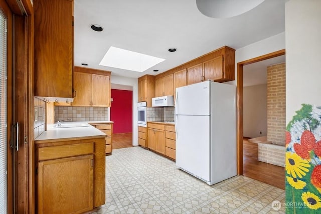 kitchen featuring decorative backsplash, a skylight, light countertops, a sink, and white appliances