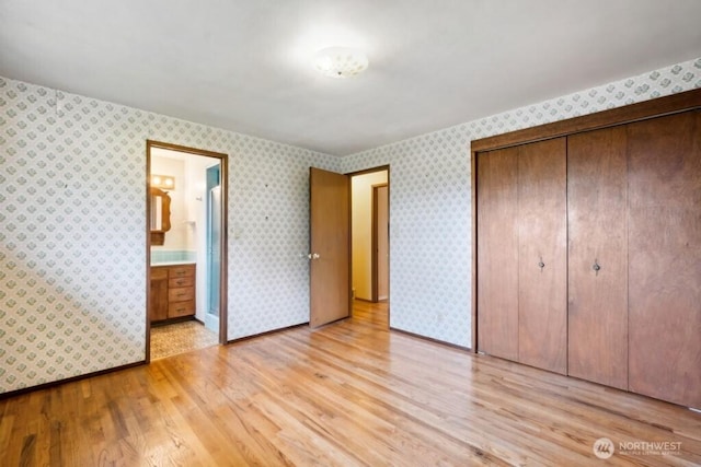 unfurnished bedroom with a closet, connected bathroom, light wood finished floors, and wallpapered walls