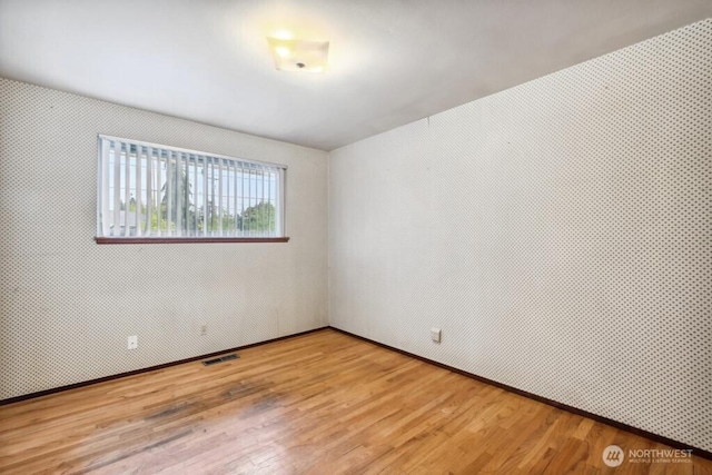 spare room with baseboards, wood finished floors, and visible vents