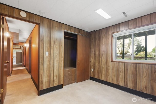 unfurnished bedroom featuring a closet, wood walls, visible vents, and light carpet