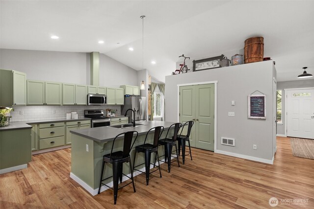 kitchen featuring green cabinetry, a breakfast bar, a sink, stainless steel appliances, and visible vents