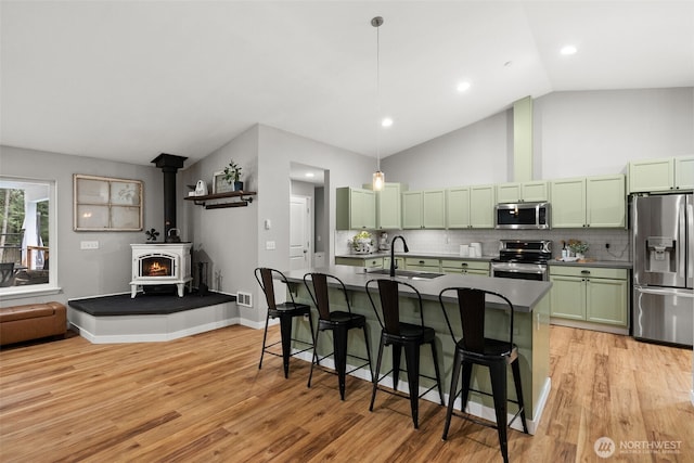 kitchen with a wood stove, dark countertops, green cabinetry, a sink, and stainless steel appliances
