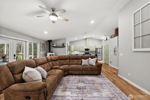 living room with ceiling fan, french doors, vaulted ceiling, a wood stove, and light wood-style flooring