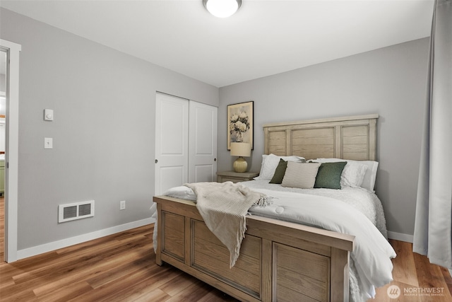 bedroom featuring visible vents, baseboards, wood finished floors, and a closet