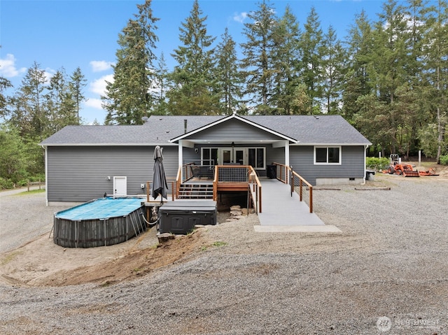 rear view of house with a deck, a pool, and roof with shingles