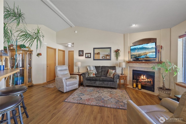 living room featuring wood finished floors, a tiled fireplace, lofted ceiling with beams, and a healthy amount of sunlight