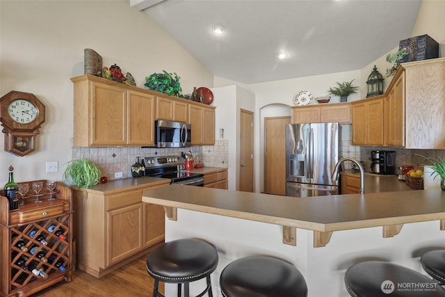 kitchen featuring a peninsula, decorative backsplash, a breakfast bar area, and stainless steel appliances