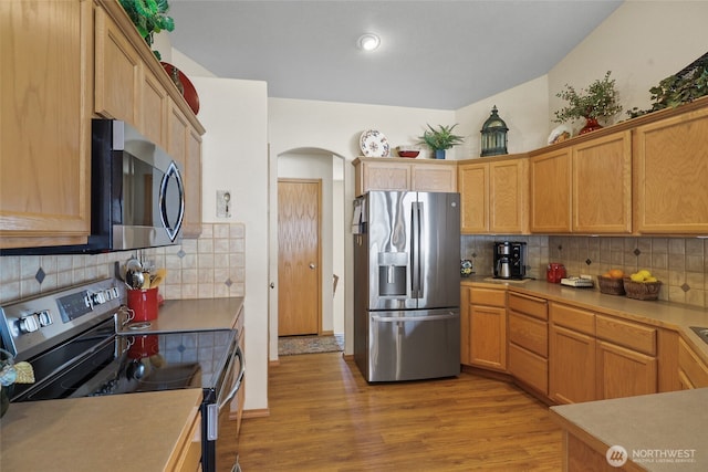 kitchen featuring light wood-style flooring, arched walkways, appliances with stainless steel finishes, and tasteful backsplash