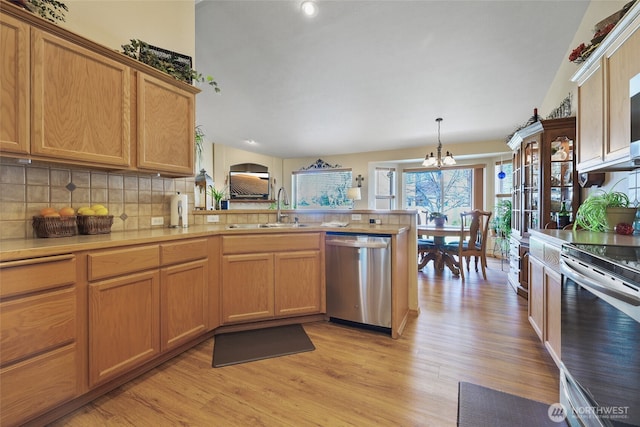 kitchen with a sink, light wood-style floors, an inviting chandelier, a peninsula, and appliances with stainless steel finishes