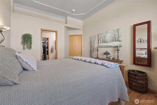 bedroom featuring a walk in closet, baseboards, wood finished floors, and a closet