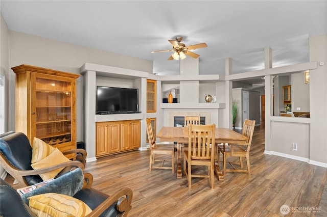 dining space with built in shelves, ceiling fan, light wood-style floors, and a tile fireplace