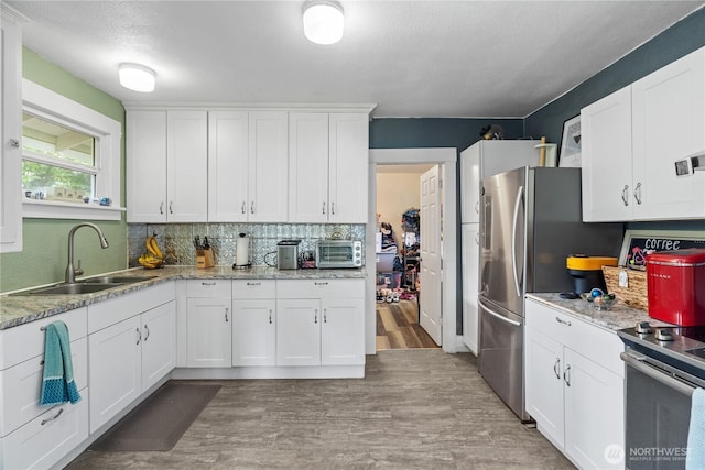 kitchen with light wood finished floors, a sink, backsplash, white cabinetry, and appliances with stainless steel finishes