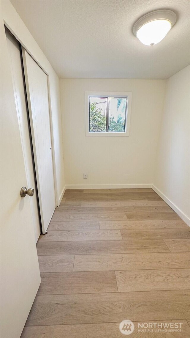 unfurnished bedroom with baseboards, a closet, and light wood-type flooring