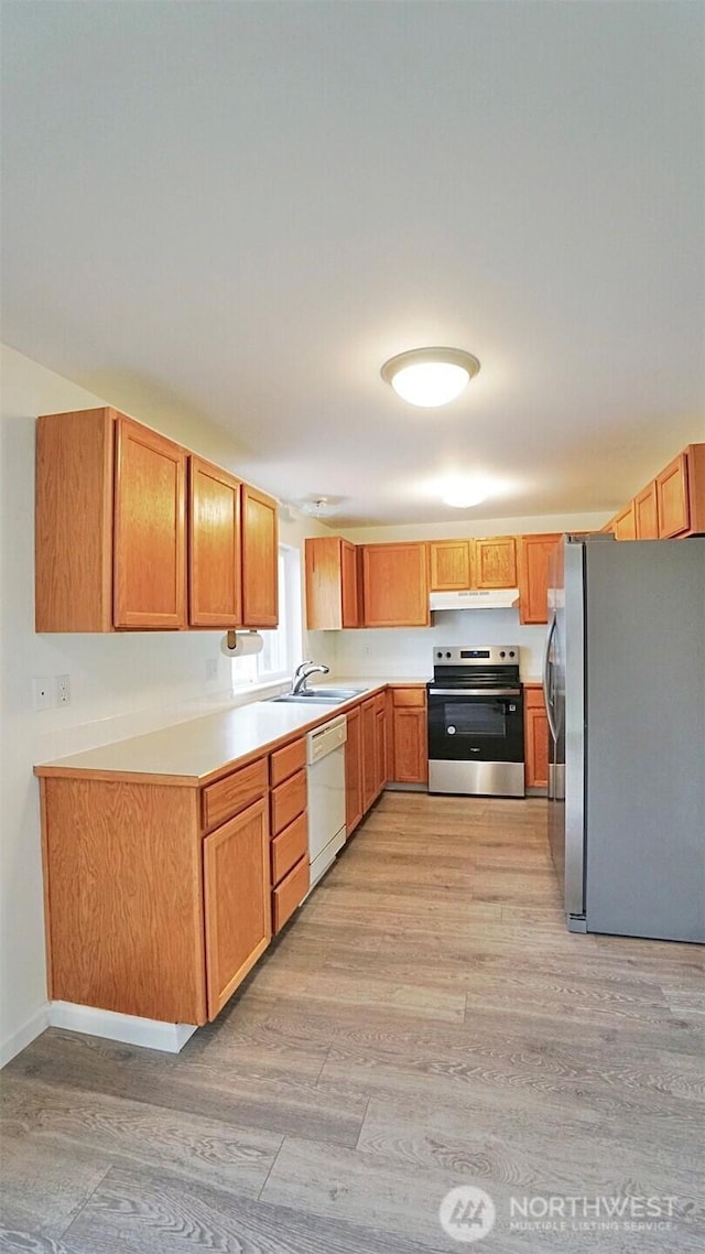 kitchen with stainless steel appliances, light wood-style floors, under cabinet range hood, light countertops, and a sink