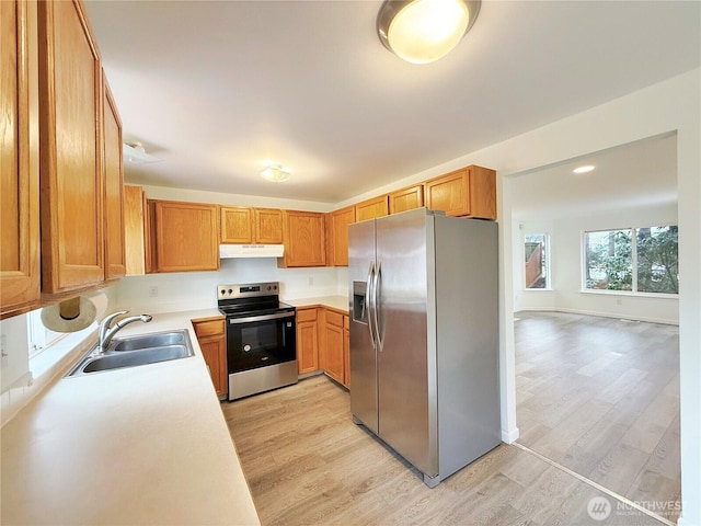 kitchen with a sink, stainless steel appliances, under cabinet range hood, light wood-type flooring, and light countertops