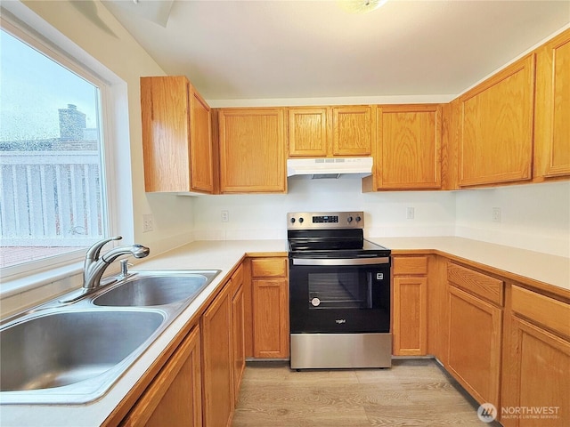 kitchen featuring light wood finished floors, a sink, under cabinet range hood, stainless steel range with electric cooktop, and light countertops