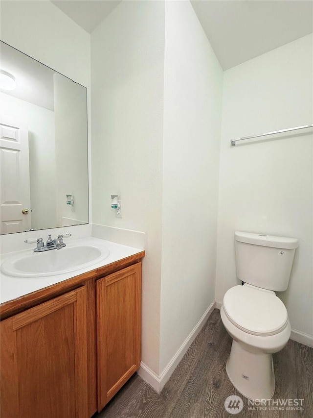 bathroom with toilet, vanity, wood finished floors, and baseboards