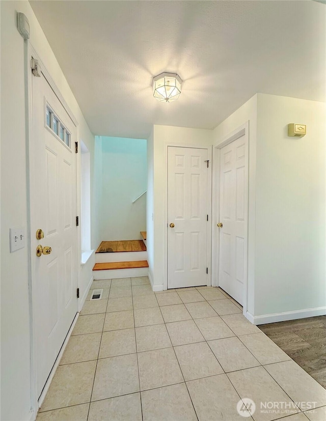 foyer featuring light tile patterned flooring, visible vents, stairway, and baseboards