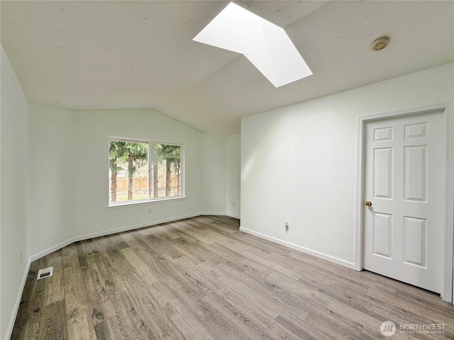 spare room with visible vents, vaulted ceiling with skylight, wood finished floors, and baseboards