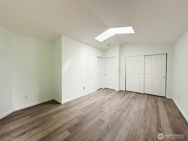 unfurnished bedroom with lofted ceiling with skylight, a closet, wood finished floors, and baseboards