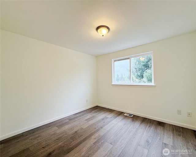 spare room featuring dark wood-style floors, visible vents, and baseboards