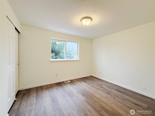 unfurnished bedroom with wood finished floors, visible vents, a closet, and baseboards