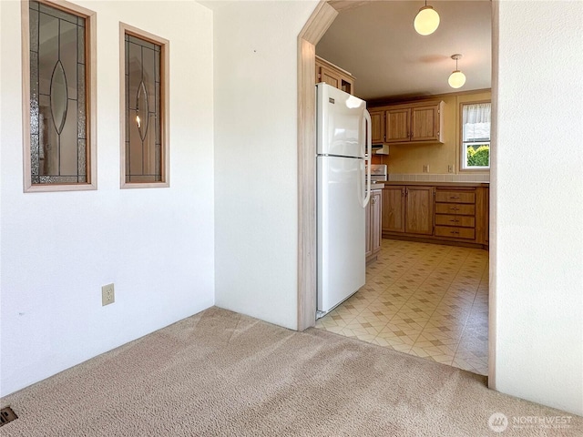 kitchen with freestanding refrigerator, light carpet, light countertops, brown cabinets, and under cabinet range hood