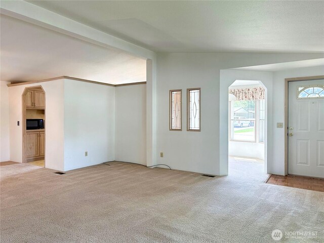 foyer entrance with light colored carpet, arched walkways, and vaulted ceiling