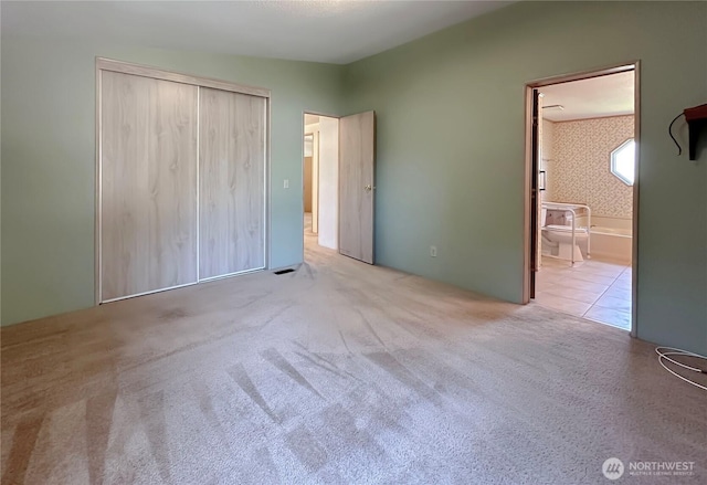 unfurnished bedroom with carpet flooring, ensuite bath, and a closet