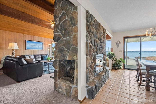 living area with tile patterned flooring, a fireplace, wooden walls, a water view, and a chandelier