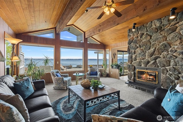 carpeted living room featuring ceiling fan, lofted ceiling with beams, a stone fireplace, wooden ceiling, and a water view