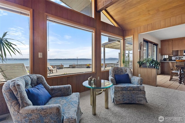 sunroom with carpet flooring, a water view, vaulted ceiling with beams, and wooden walls